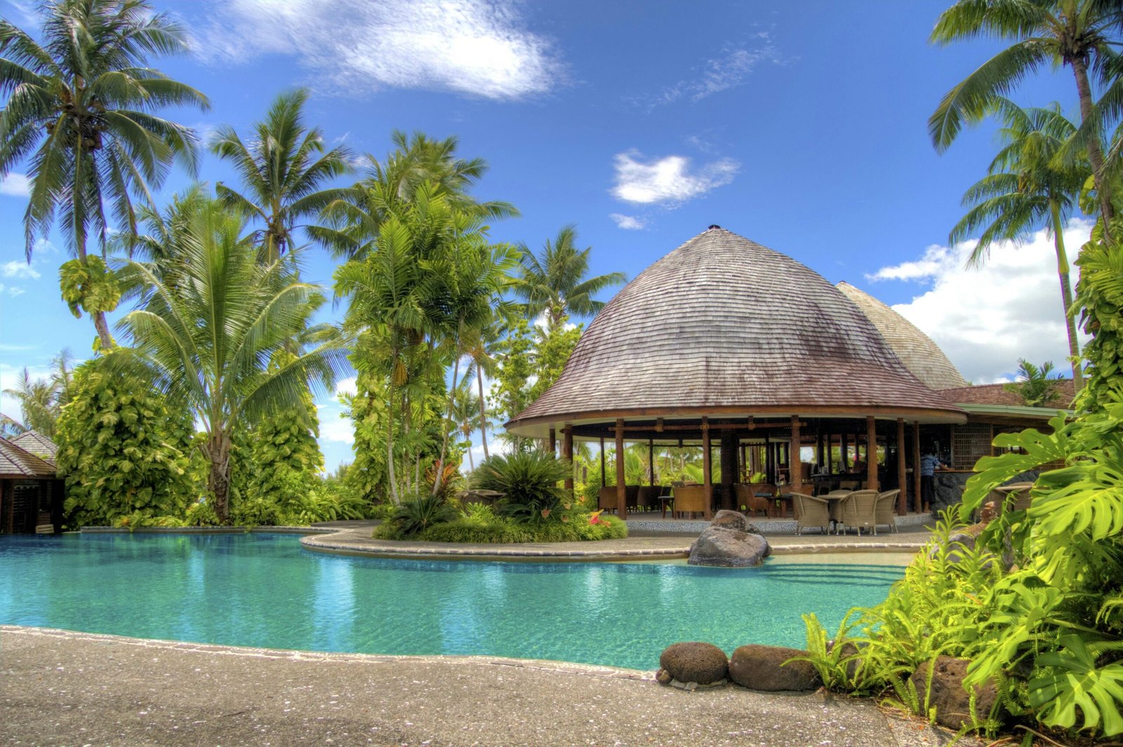 Luxurious tropical resort with a serene pool, lush palm trees, and relaxation area.